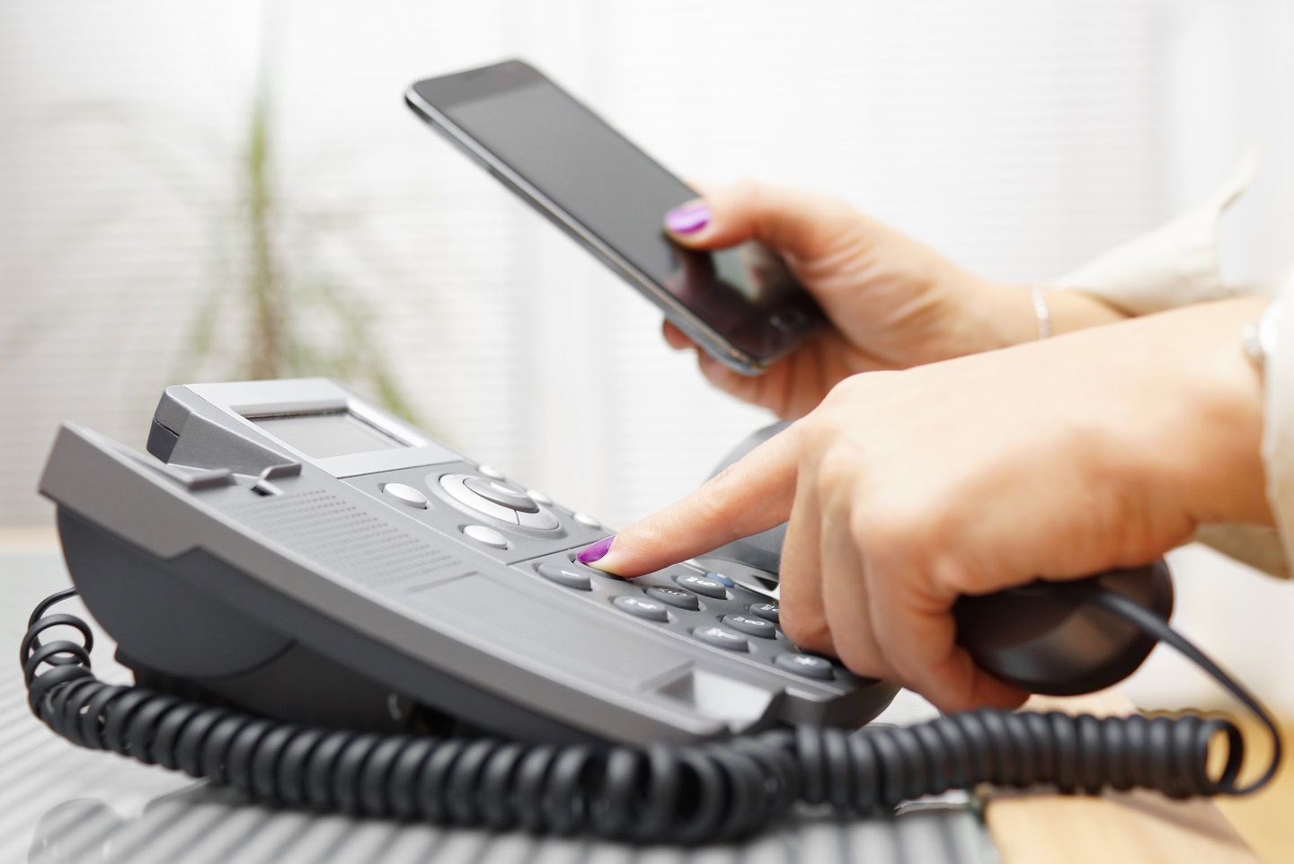 Adobe Stock Photo - Woman using landline and looking at cell phone 