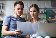 Couple sitting on the couch, looking at utility bills and a laptop