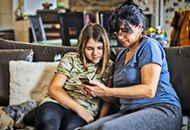 Woman and teenage daughter on the couch, looking at a mobile phone