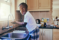 Young boy on stepstool washing hands in kitchen sink