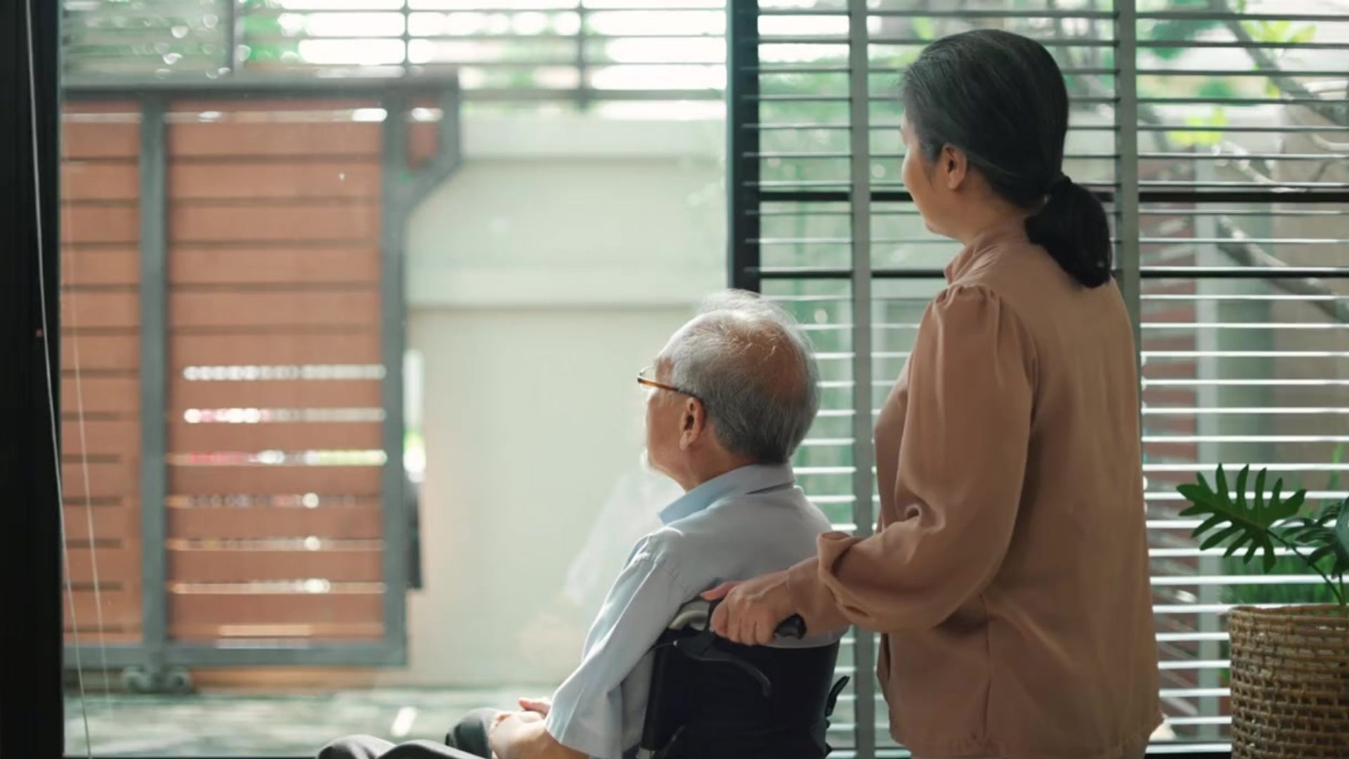 Mature Asia couple. The husband is in a wheelchair, and the wife is standing behind him and chatting with him.