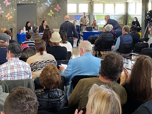 A view of the speaker's table taken from the back of the room. There are many people in attendance.